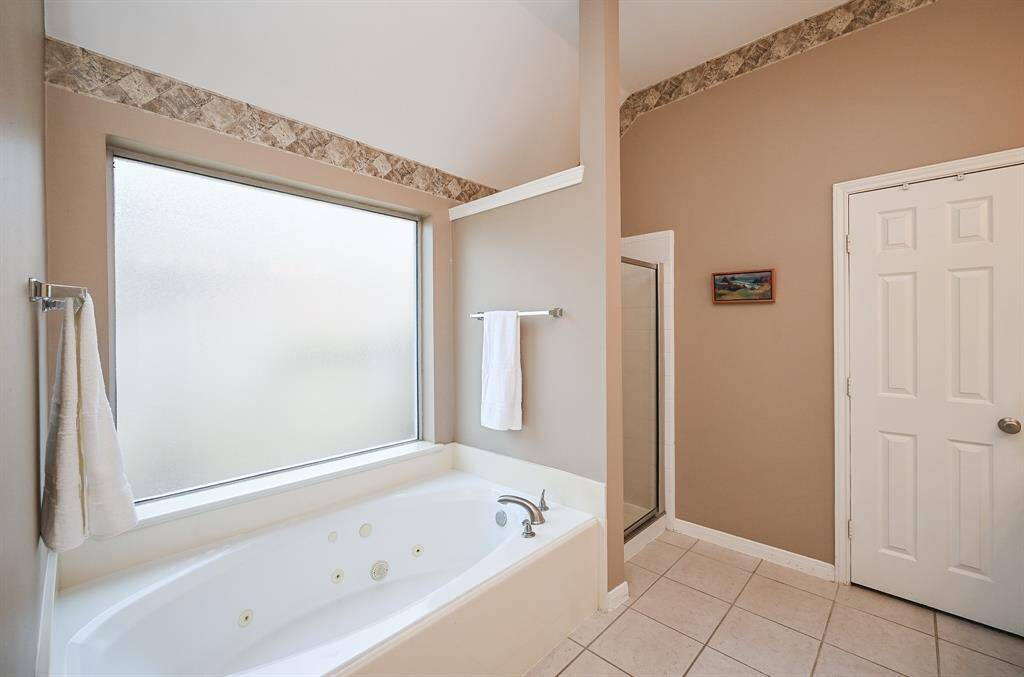 The bathroom also features a large soaking tub under a frosted privacy window, a separate walk-in shower, and a private water closet—designed for both function and relaxation.