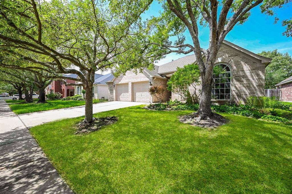 Attractive curb appeal with a well-maintained front yard, shaded by large oak trees and framed by a quiet, tree-lined street.