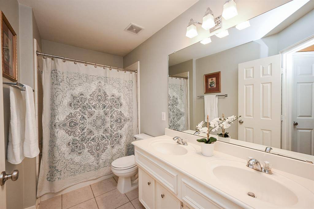 Spacious secondary bathroom with double sinks, neutral tile flooring, and a full tub & shower combination.