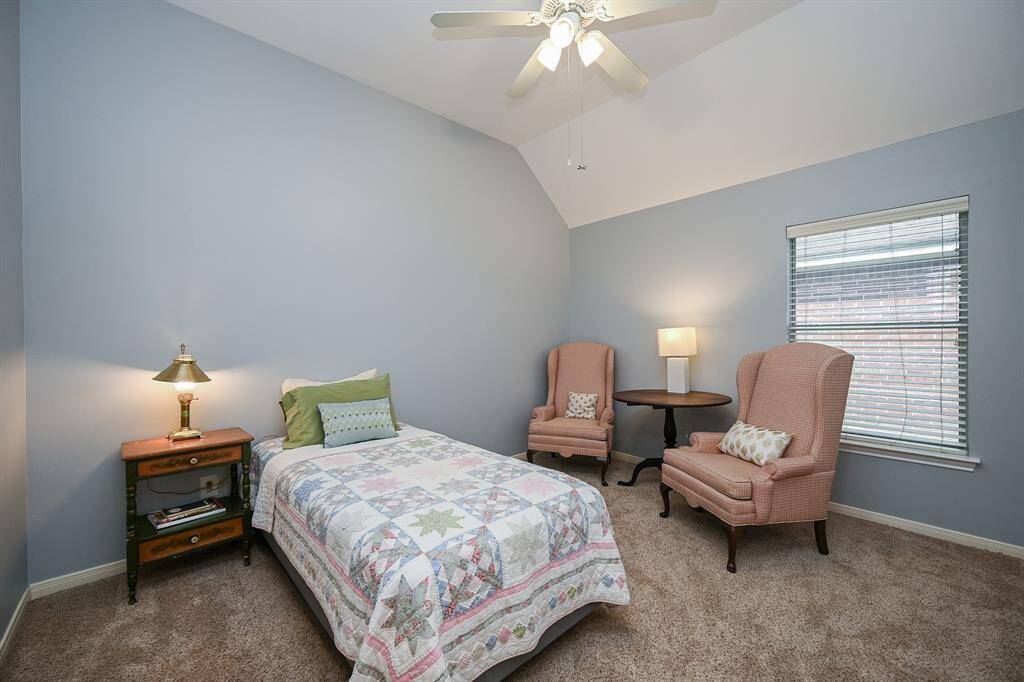 Light-filled secondary bedroom with vaulted ceilings and plush carpeting, offering a versatile space for sleep or study.