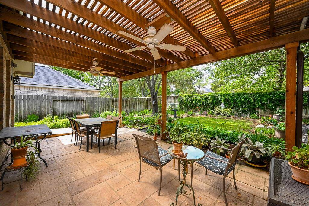 Enjoy a spacious covered patio featuring a wood pergola ceiling, ceiling fans, and views of a lushly landscaped backyard.