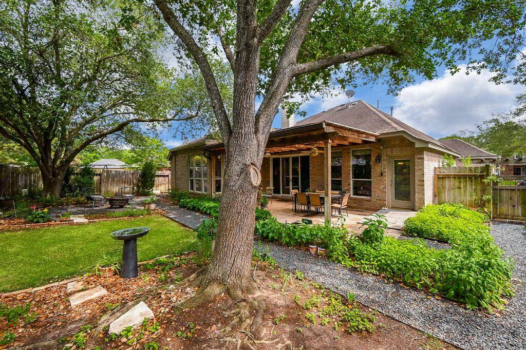 The backyard showcases a mature tree canopy, gravel pathways, and seamless flow to the covered patio.