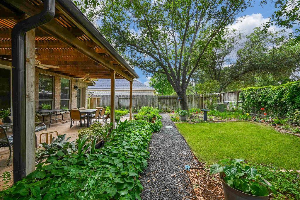 A gravel garden path leads to the covered patio, surrounded by greenery and bordered by vibrant flower beds.