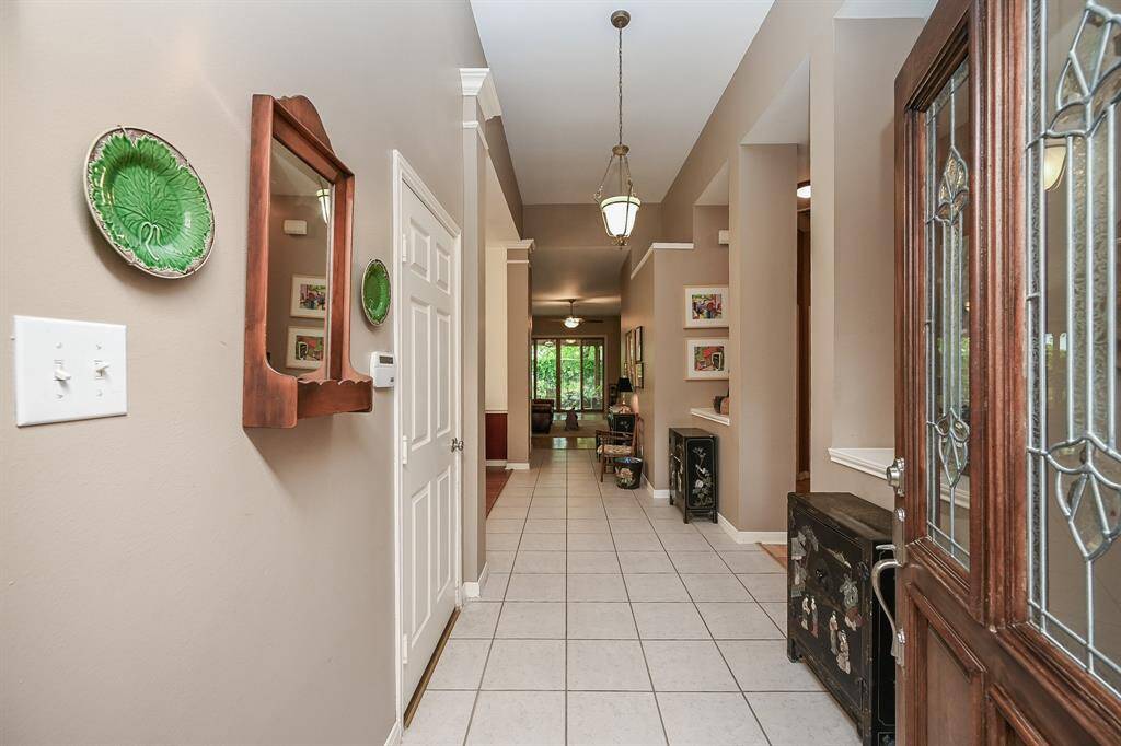 The foyer opens to a long, elegant hallway with high ceilings, crown molding, and tile floors that lead into the main living areas.