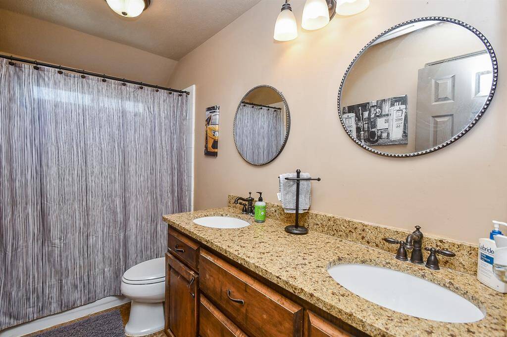 This bathroom features a double vanity with granite countertops, two oval mirrors, and stylish lighting. It includes a step-in tub shower