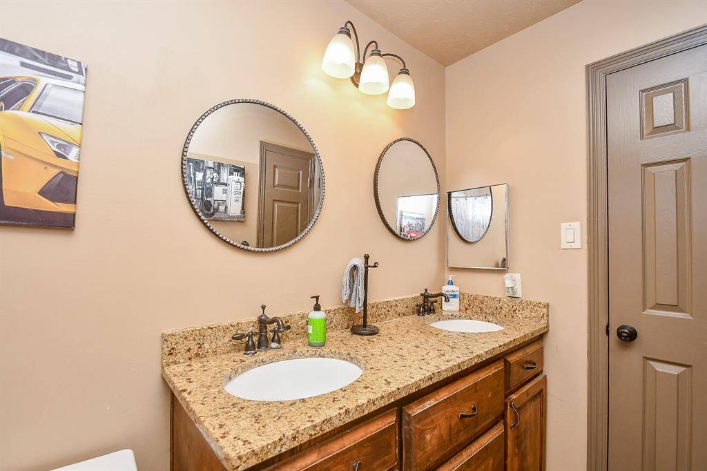 This bathroom features a double vanity with a granite countertop. The wood cabinetry offers ample storage.