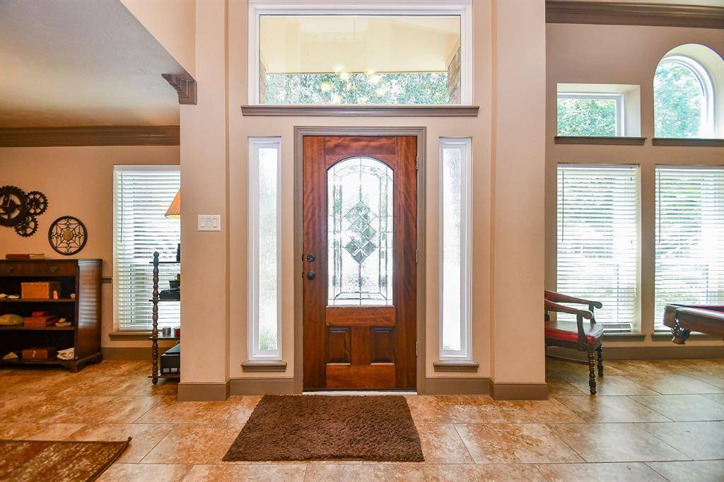 This welcoming entryway features a wooden front door with decorative glass panels, surrounded by tall side windows. The space is bright, with ample natural light, giving it a cozy and elegant feel.