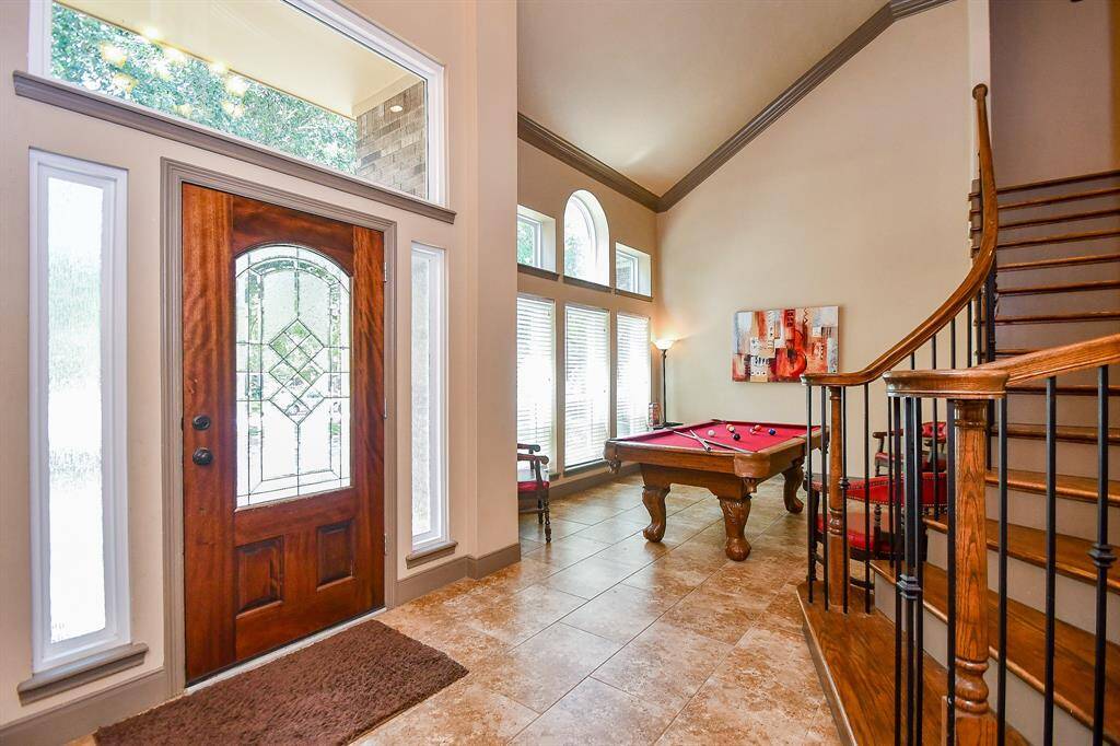 This inviting entryway features a decorative wooden front door with sidelights, leading into a spacious formal living/entertainment room with high ceilings. The room includes a stylish curved staircase and is highlighted by large windows for natural light.