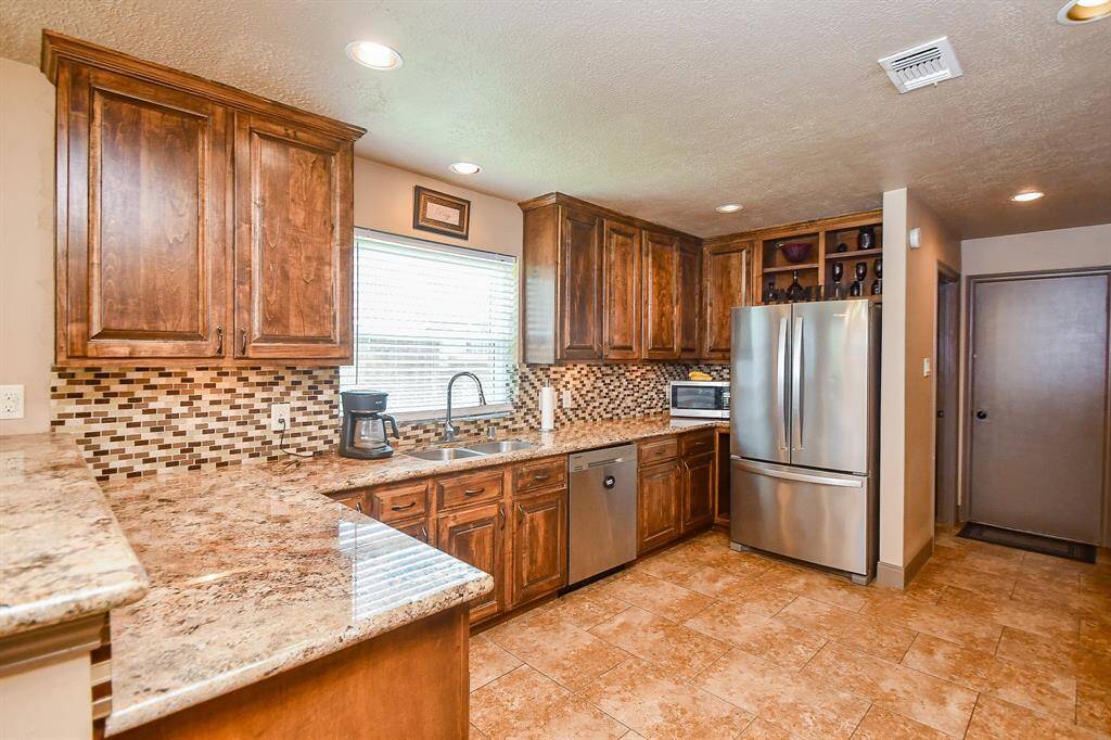 This kitchen features warm wooden cabinets, a stylish tile backsplash, and granite countertops. It includes stainless steel appliances, ample storage, and a window for natural light. The tile flooring complements the overall design, creating a welcoming space.