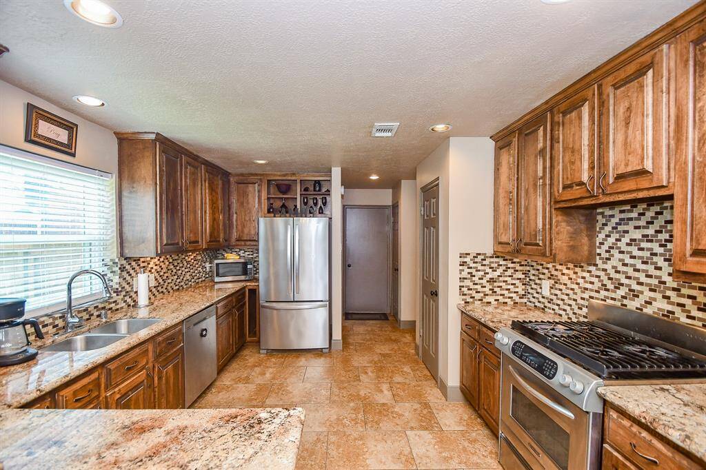 This kitchen features warm wood cabinetry, modern stainless steel appliances, and a stylish tile backsplash. It offers ample counter space, a double sink, and a cozy, functional layout with plenty of natural light.