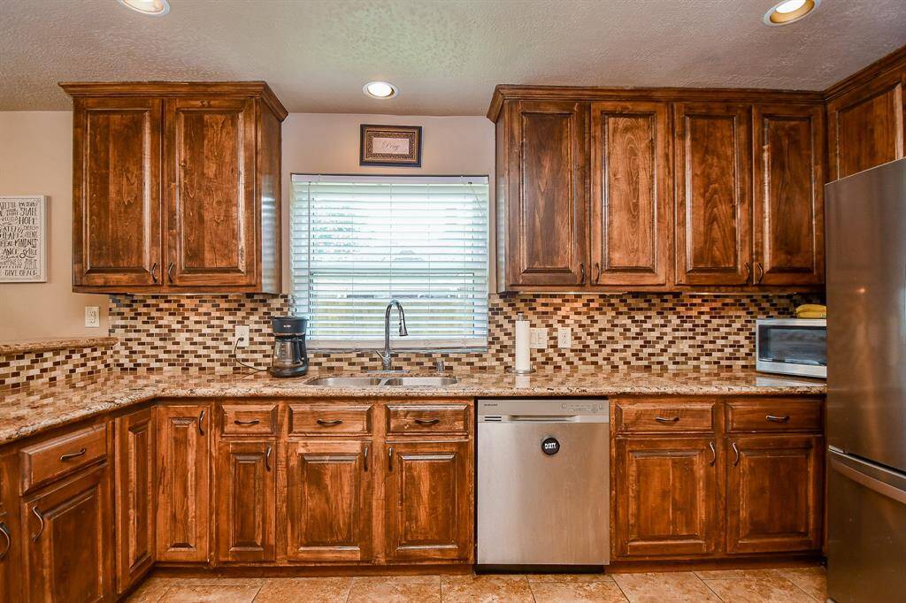 The kitchen features rich wood cabinetry, a stylish mosaic tile backsplash, and stainless steel appliances, offering a warm and inviting atmosphere.