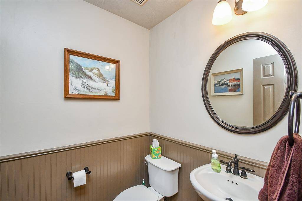 A cozy half-bathroom featuring a pedestal sink and partially paneled walls.