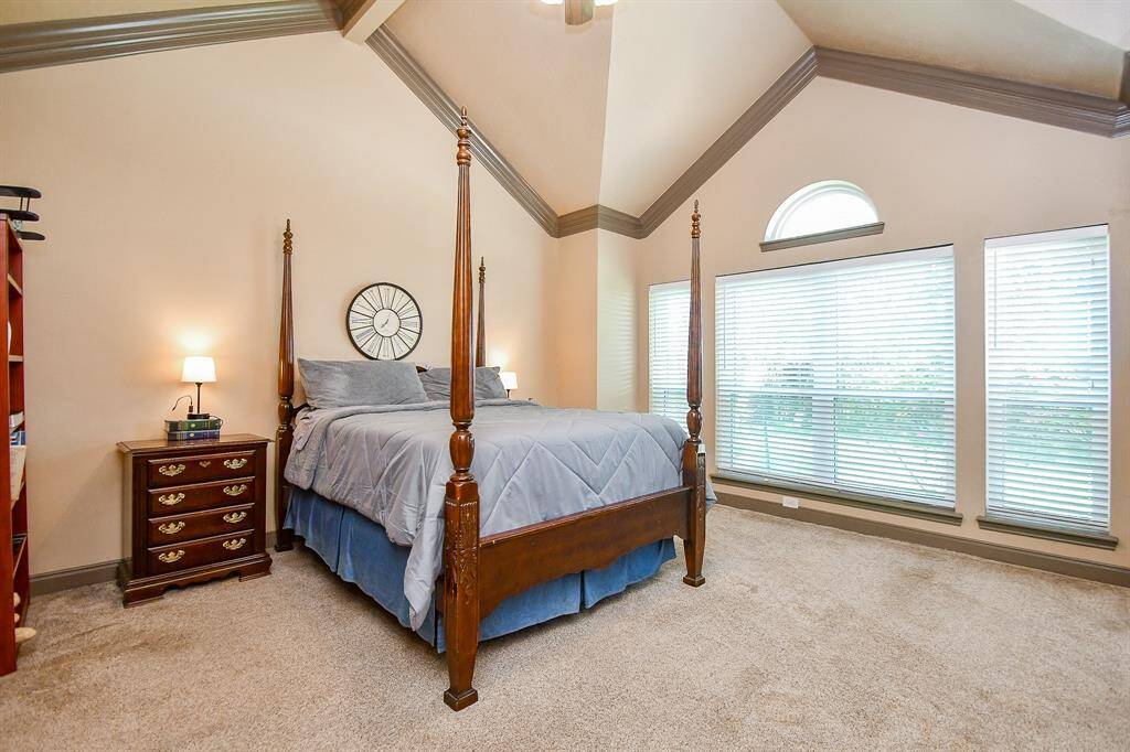 This spacious bedroom features a vaulted ceiling, large windows with ample natural light. The room has is elegant yet offers a warm and inviting atmosphere.