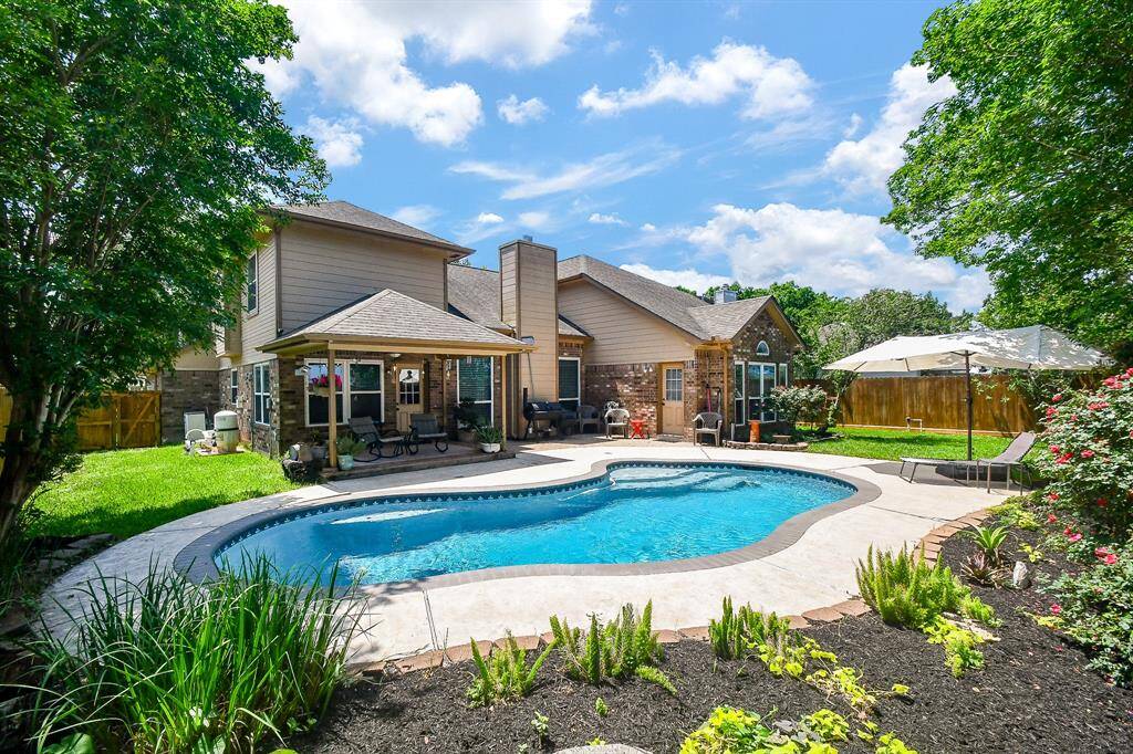 This inviting backyard features a spacious pool surrounded by lush greenery and a patio area perfect for relaxing or entertaining. The two-story home has a cozy covered patio complementing the serene outdoor space.