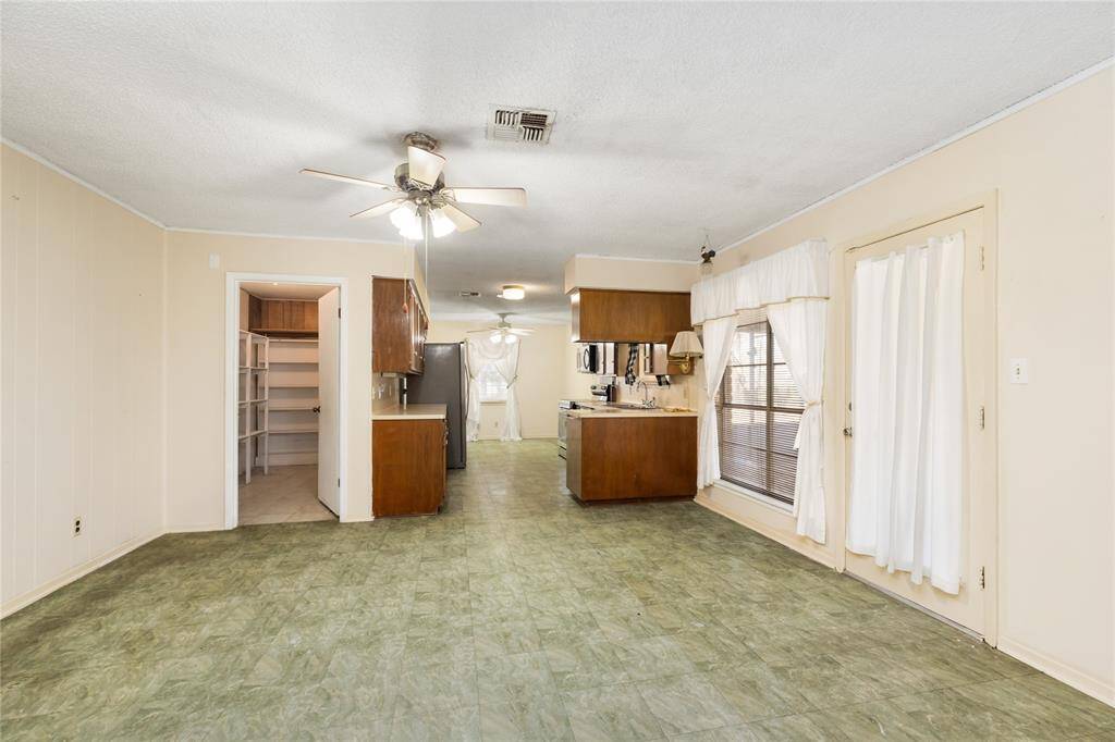 A spacious open-concept kitchen and living area with light-color walls creates a bright and welcoming atmosphere. The kitchen offers warm wooden cabinetry, a refrigerator, and generous counter space for cooking and entertaining. Large windows fill the room with natural light. A convenient pantry with built-in shelves offers extra storage for every day essentials.