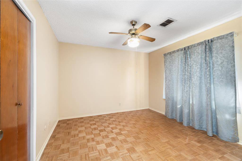 This inviting room boasts classic parquet flooring, neutral walls, and a ceiling fan for added comfort, and the large window fills the space with natural light.