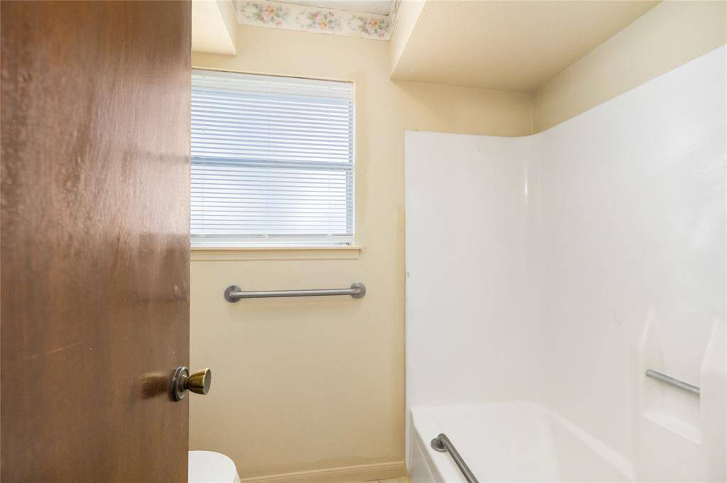 This bathroom offers a functional and inviting space with a shower-tub combo surrounded by crisp white detailing. A window allows natural light to brighten the room, while safety grab bars provide added convenience. Neutral-toned walls create a calming atmosphere.