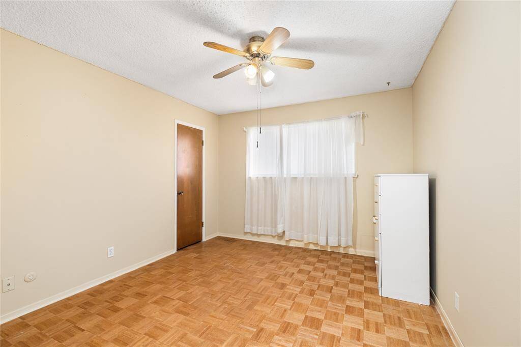 Continuing through the home, you step into this bright and airy room, where the charming parquet flooring continues, adding warmth and character. A ceiling fan enhances comfort, while neutral walls provide a versatile backdrop, which is further enhanced by the natural light provided by the large window.