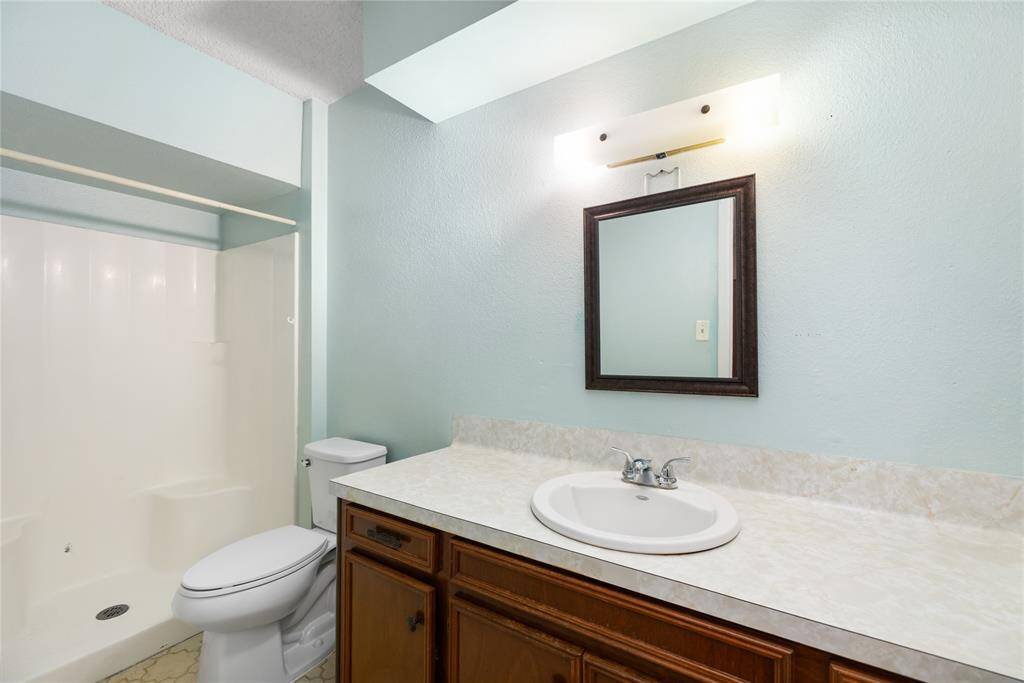 This bathroom showcases a fresh, simple design with light aqua walls that add a touch of tranquility. A single vanity with a mirror offers functionality, while a classic wood cabinet provides warmth and charm. The walk-in shower and ample counter space complete the room, creating a bright and inviting atmosphere.