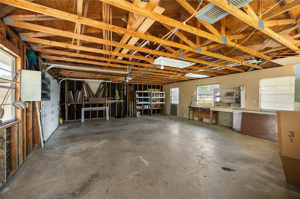 This spacious garage features exposed wooden beams, ample natural light from multiple windows, and plenty of room for storage or projects. It includes built-in shelving, workbenches, and a concrete floor, making it ideal for a workshop or additional storage space.