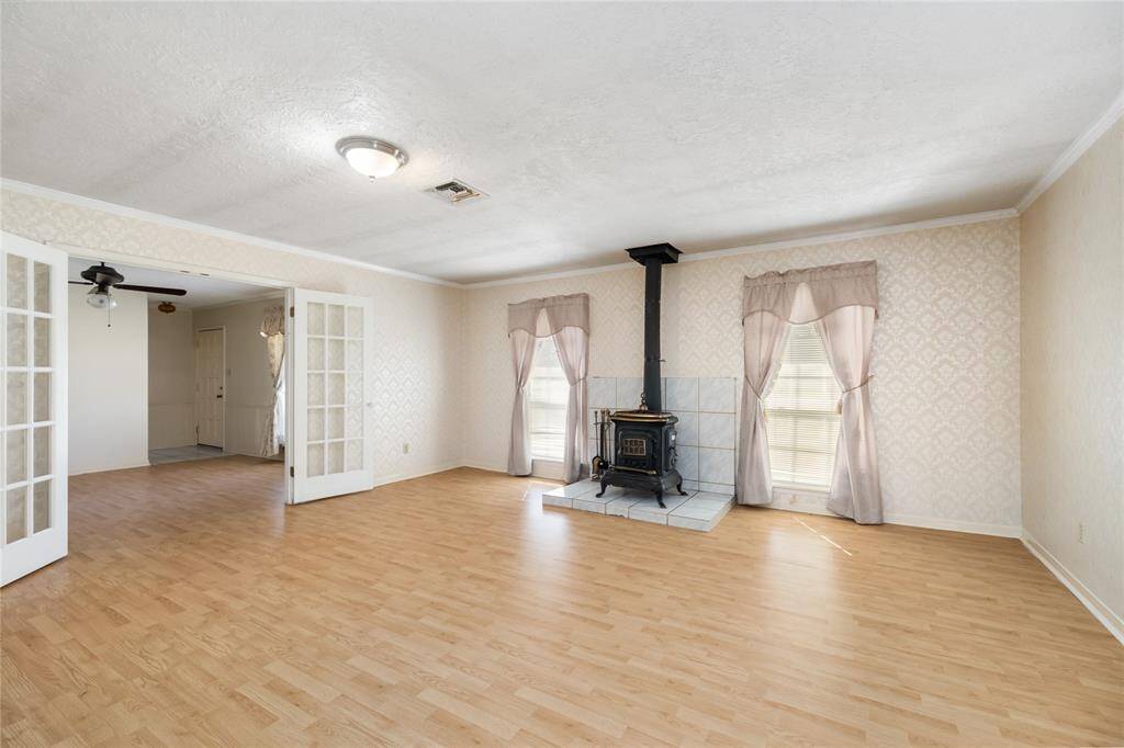 This living room features a cozy wood-burning stove, light hardwood floors, and elegant French doors leading to another room. The space is bright with natural light from two windows, and has a neutral color palette - perfect for personalization.