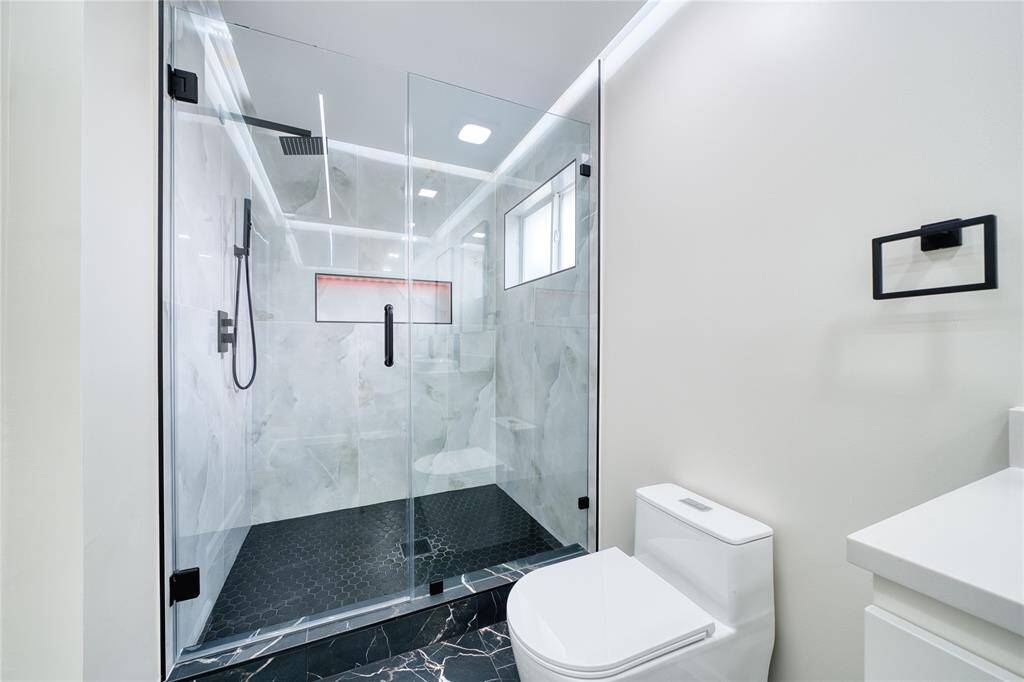 Oversized shower features rain shower head, hand held shower, porcelain tile and shampoo box.