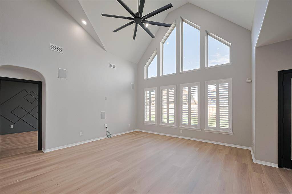 This spacious room features high vaulted ceilings, a modern ceiling fan, and large floor-to-ceiling windows with shutters, allowing ample natural light.