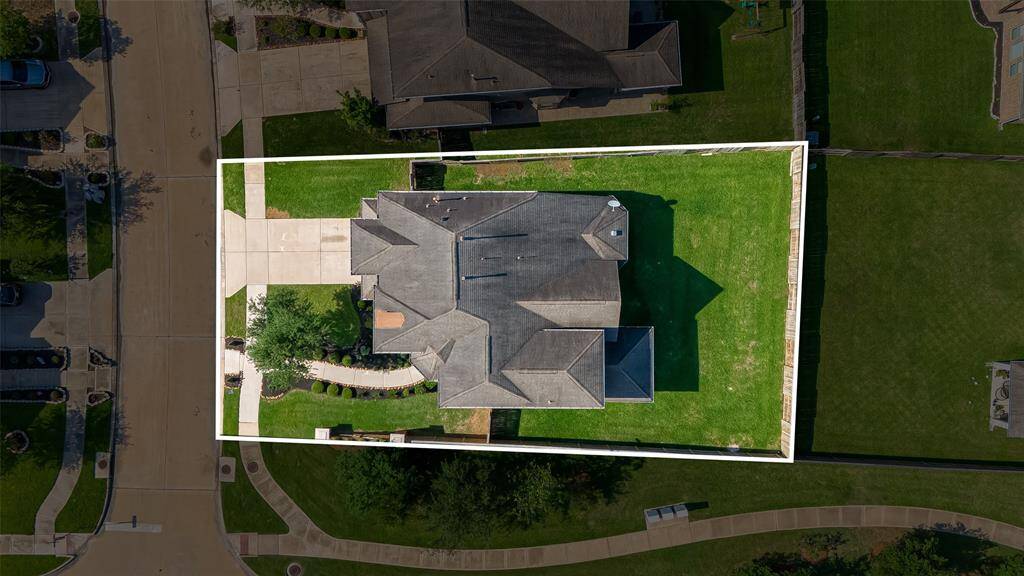 This aerial photo shows a well-maintained home with a spacious yard, situated on a corner lot. The property features a large driveway, landscaped pathways, and is bordered by sidewalks.