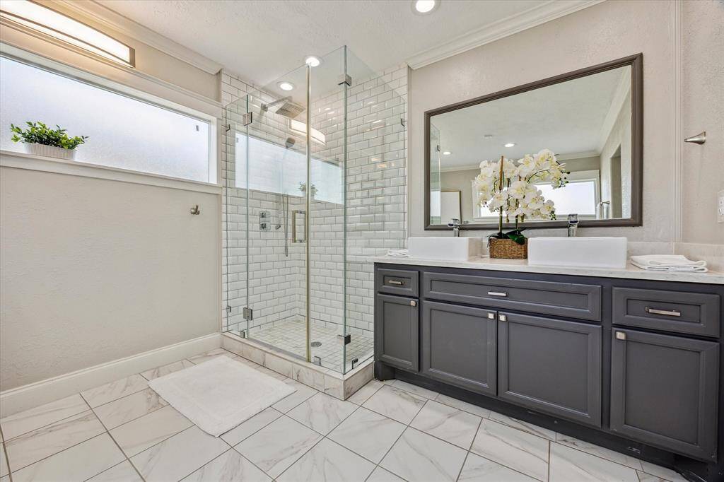 The spa-inspired primary bath features a frameless glass walk-in shower with subway tile surround, double vessel sinks, quartz countertops, and a rich charcoal vanity—perfectly blending modern elegance with everyday function.