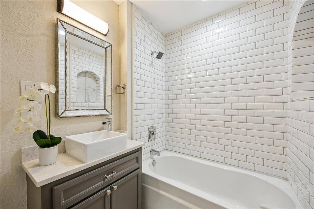 This updated secondary bathroom showcases a sleek vanity with vessel sink, framed mirror, and a classic subway tile tub/shower combo with built-in niche—offering style and functionality in every detail.