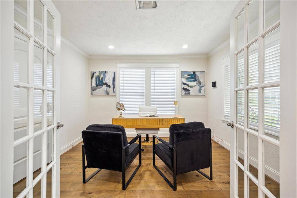 One of two secondary bedrooms, this light-filled space is currently staged as a home office. Features include hardwood floors, elegant crown molding, and recessed can lighting that enhances the clean, modern aesthetic.