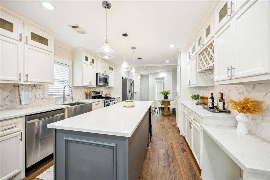 Bright and beautifully updated, this kitchen features a large center island with seating, elegant glass pendant lighting, and an abundance of cabinetry—including a built-in wine rack and serving area—perfect for entertaining or everyday ease.
