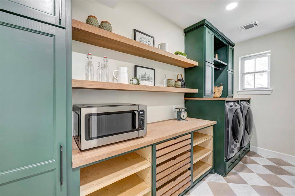 The butler’s pantry features sleek floating white oak shelves, sliding drawers, and built-in electrical outlets—perfect for charging cordless vacuums and keeping essentials organized. Thoughtfully tucked away, this space helps maintain a clutter-free home. The laundry area is equally well-designed, with washer and dryer units and convenient pull-out storage, making laundry day effortless.