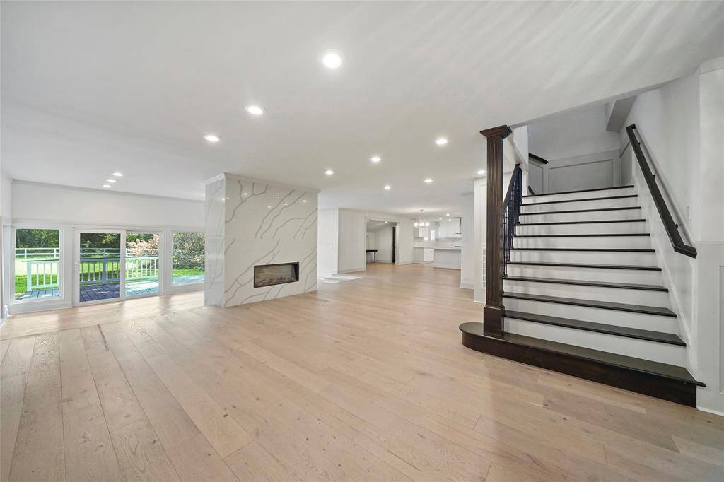 Sleek white fireplace with black trim, sliding glass doors leading to a patio, and a striking dark wood staircase with white treads and black risers. The staircase also features a dark wood handrail and black railing, adding a sophisticated touch to the room.