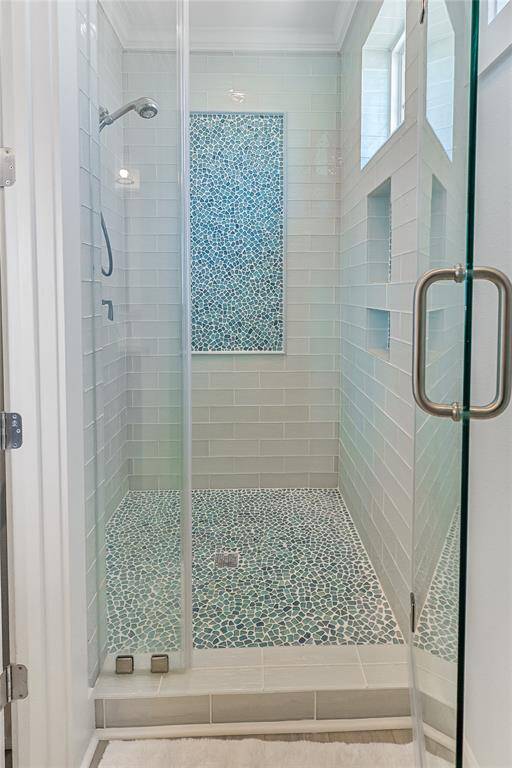 The primary ensuite features a stunning glass-enclosed shower with vibrant coastal tile work, adding a playful yet elegant touch to the home's coastal charm. This spa-like retreat perfectly blends style and relaxation.
