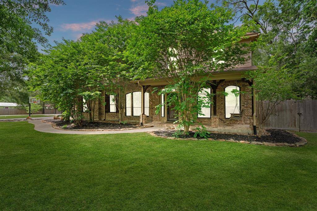 Charming two-story brick home with arched windows, a covered front porch, and lush mature landscaping. Features a curved walkway, spacious manicured lawn, and a private fenced yard with a basketball hoop. The house, specially at twilight, oozes with comfort and familiarity.