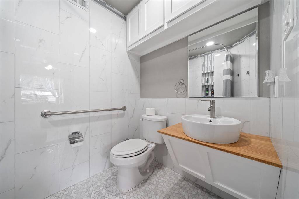 The separate suite features a fully equipped bathroom with glass tiles, designed for space efficiency. It includes a light wooden sink top paired with white cabinets, creating a versatile floating vanity.