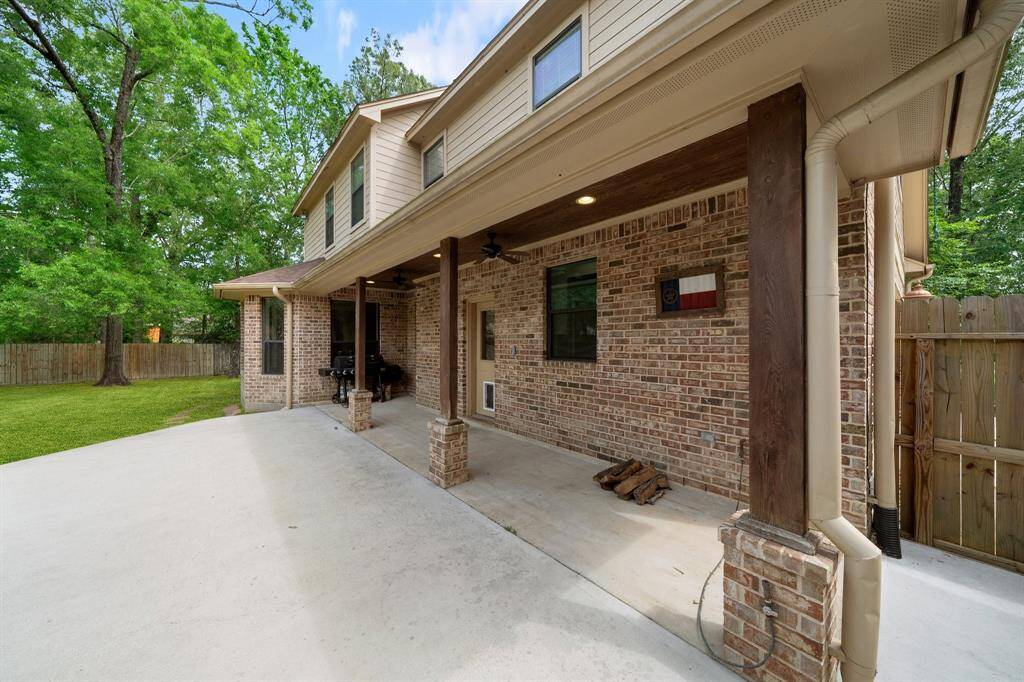 The covered patio with a brick wall and sturdy wooden columns creates a charming and durable outdoor space perfect for those beautiful afternoons surrounded by trees.
