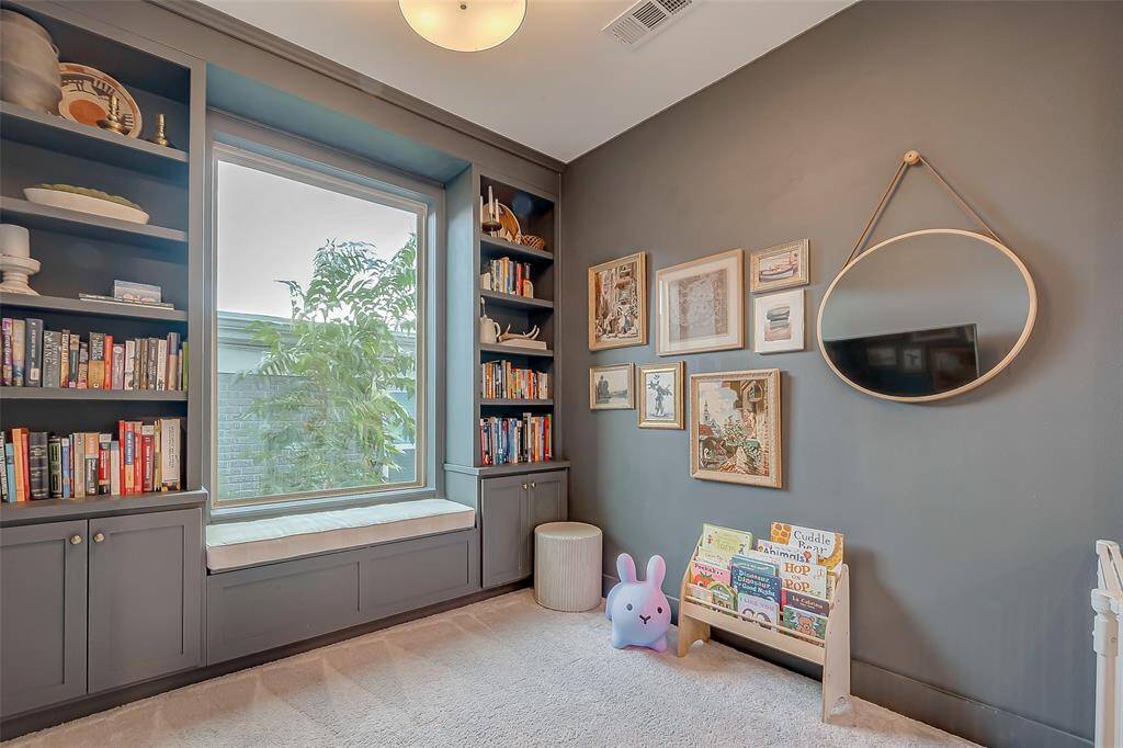 This is an elegant Office area with built-in bookshelves, a comfortable window seat, with a pleasant view outside, creating a charming and inviting atmosphere. Currently is being used as a well-lit playroom, reading nook.