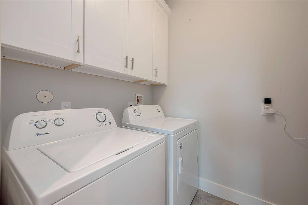 The photo shows a dedicated laundry space with both gas and electric connections, and overhead white storage cabinets, providing a functional and tidy area for household chores.