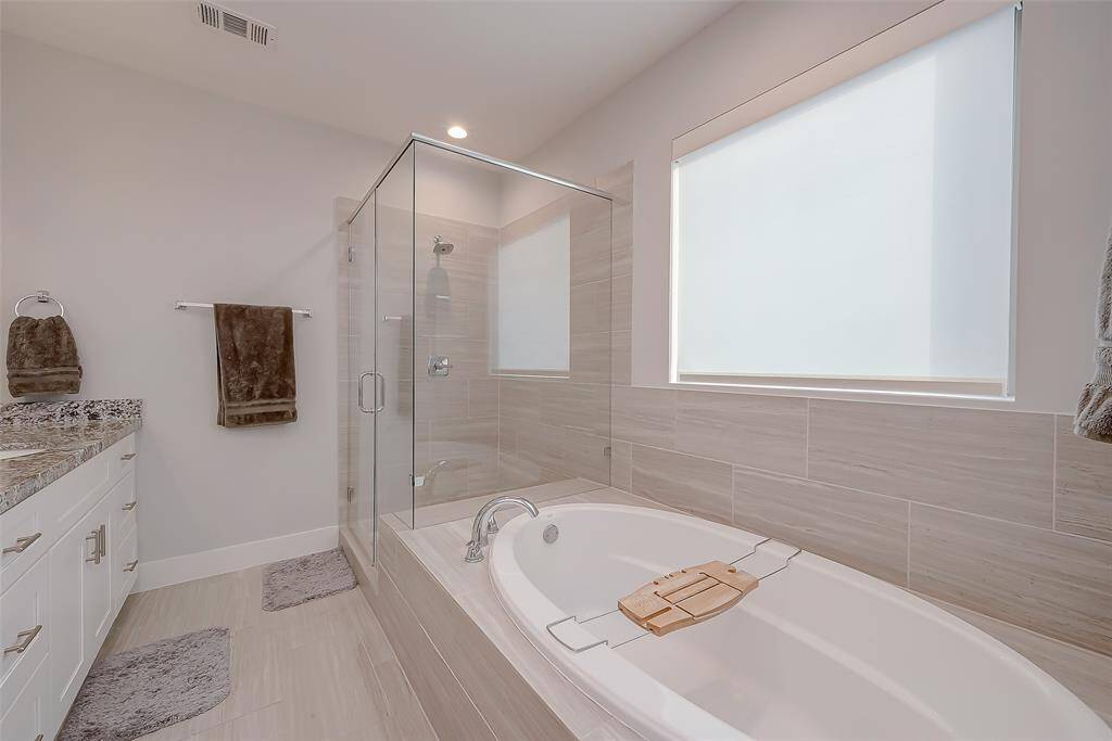 This is a modern bathroom featuring a granite countertop with 2 under-mount sinks , a large framed mirror, a glass-enclosed shower, and a separate oversized bathtub. The room has neutral tones with tile flooring.