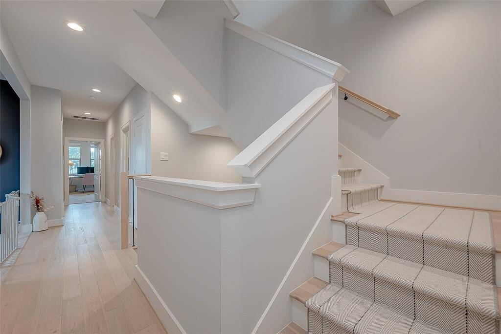 The hallway is open airy, filled with natural lighting from perfectly placed windows, featuring recessed lighting and light hardwood flooring in the hallway and the risers in the stairwell.  The home showcases a classic clean, neutral color palette throughout.
