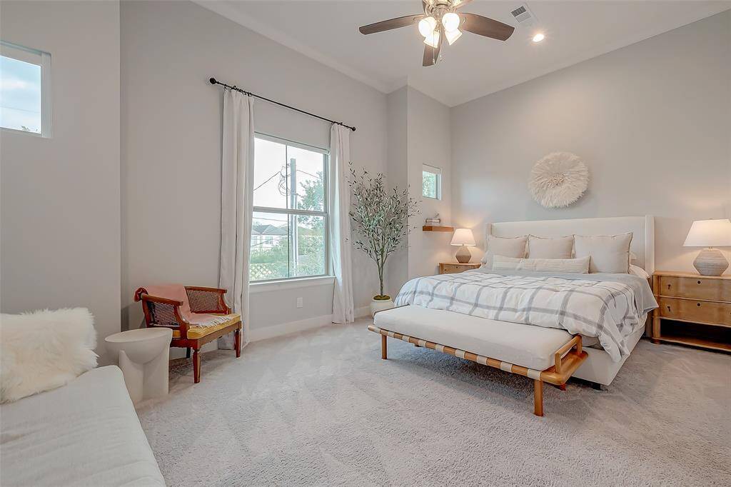 This Primary Bedroom is a bright and airy, featuring High Ceilings, Crown Molding all done in neutral colors. For extra comfort a ceiling fan, plush carpeting, and a window allowing for natural light. Spacious primary room creating a cozy and inviting space.