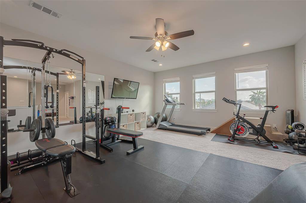 This is a spacious, multi-purpose room currently set up as a home gym, and is a great space for a game room. Featuring a ceiling fan, and lots of natural light. There's a visible doorway leading to an adjoining bedroom.