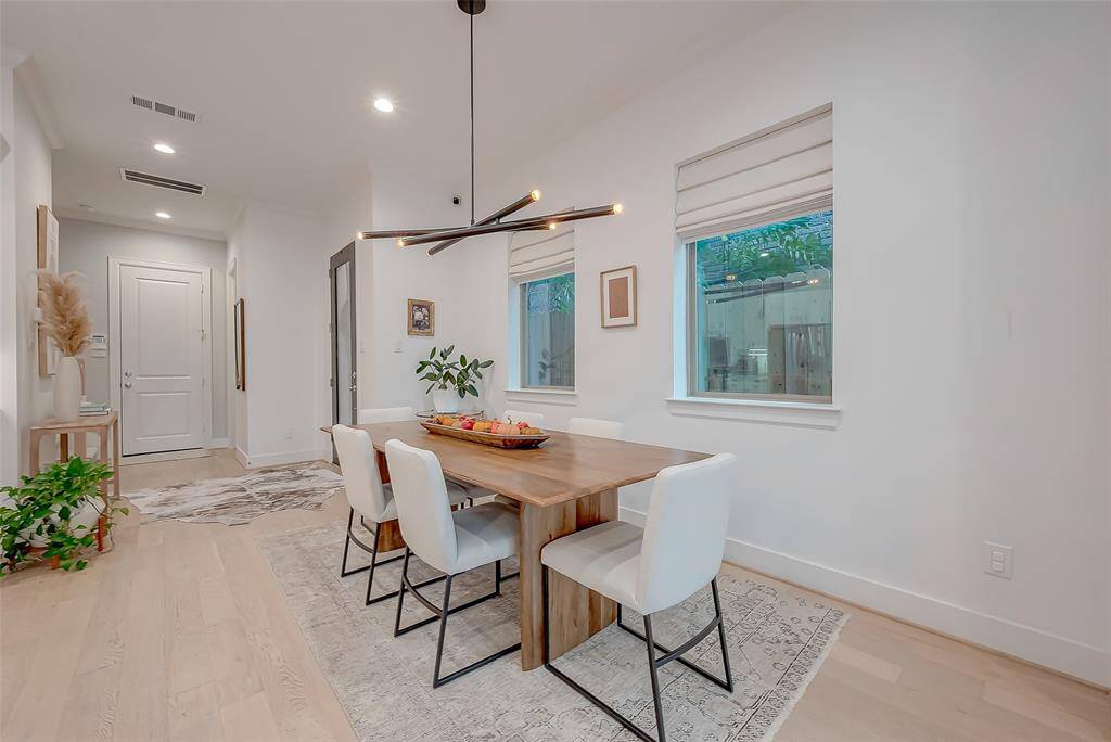 This is a spacious and well-lit dining area adjacent to a cozy living space, featuring modern lighting, hardwood floors, and large windows that provide ample natural light. The open floor plan allows for seamless entertaining and comfortable living.