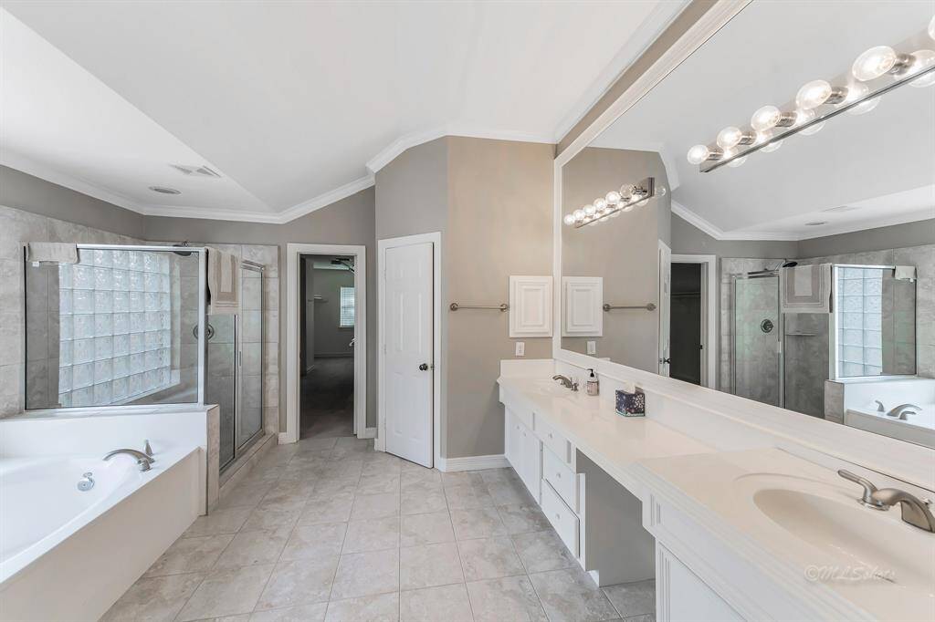 The en suite bathroom features studio lighting, dual vanities, crisp white cabinets, nickel finish hardware, jetted garden tub, and an over-sized shower with a rain shower head.