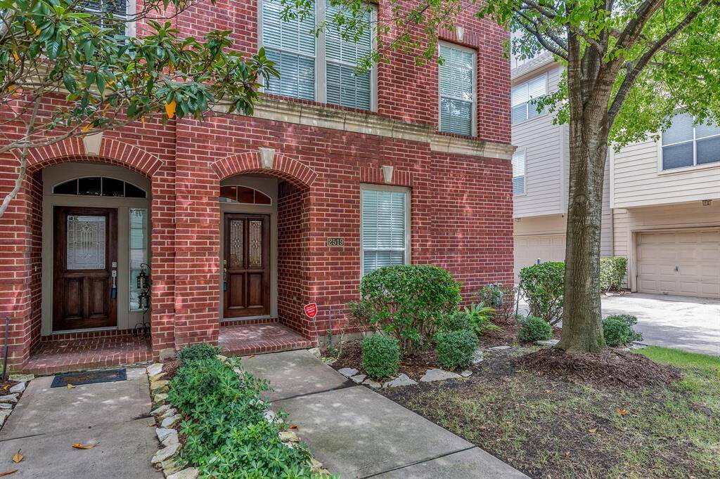 This home features a traditional red brick exterior, green space at the front of the home, a charming pathway to the front door, a beautiful wooden door, and transom windows.