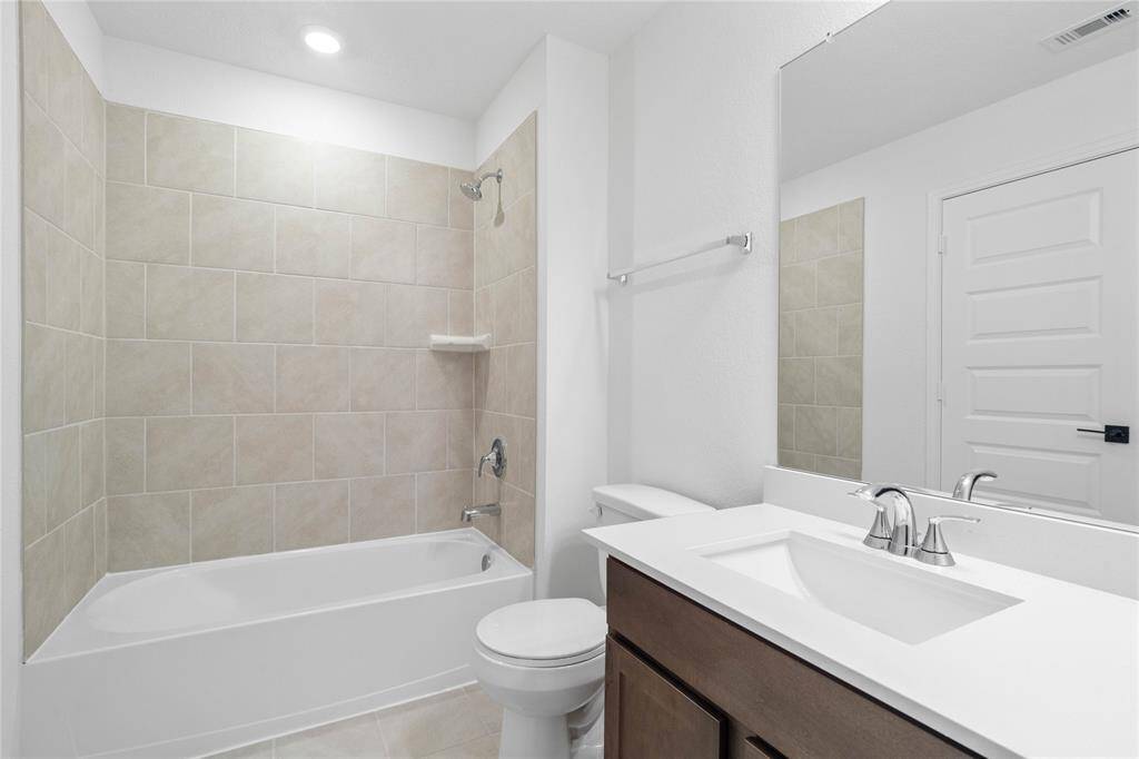 Secondary bath features tile flooring, tub/shower combo with tile surround, stained wood cabinets, beautiful light countertops, mirror, sleek fixtures and modern finishes.