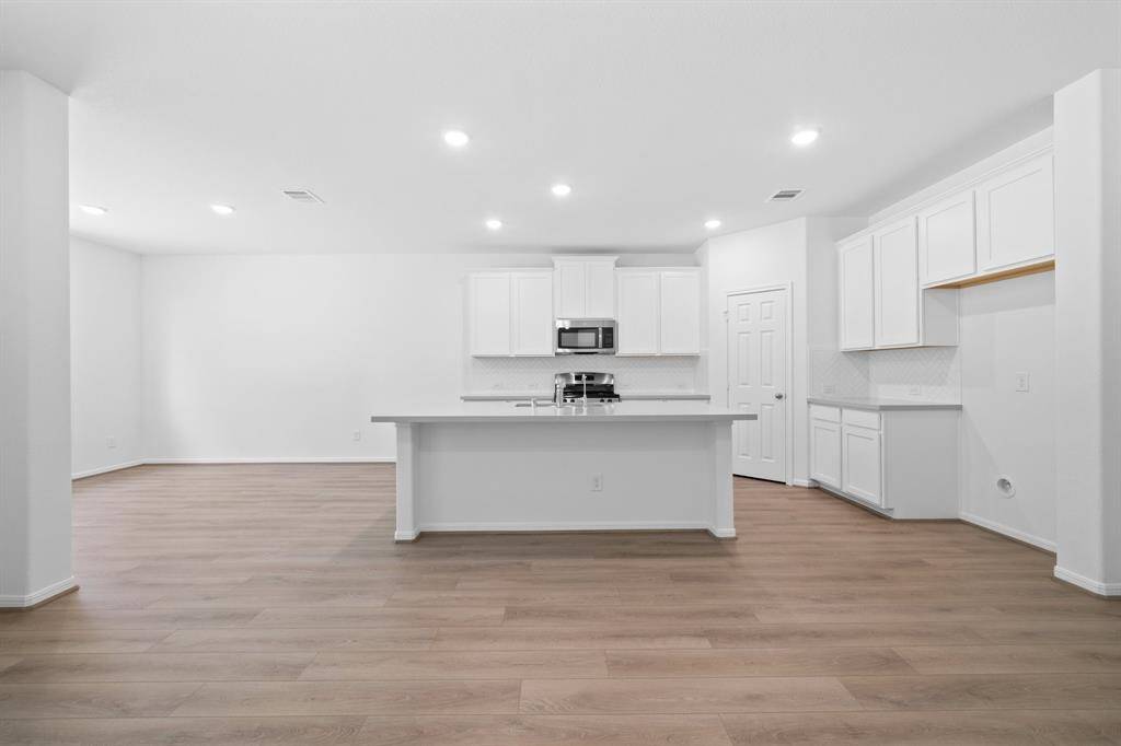 This light and bright kitchen features a large quartz island, white cabinets, a large sink overlooking your family room, recessed lighting, and beautiful backsplash.