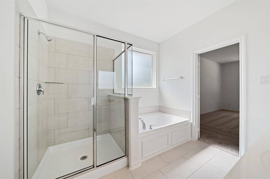This additional view of your primary bathroom features tile flooring, fresh paint, walk-in shower, a separate garden tub, and a large walk-in closet.